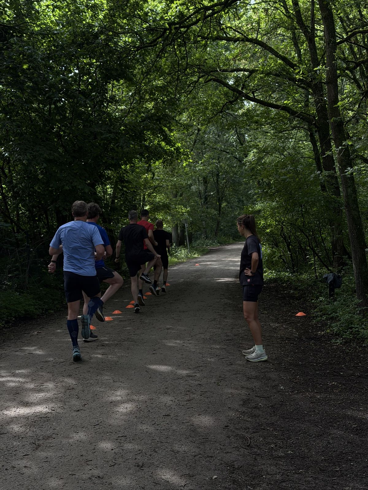 Groep lopers doet loopscholing langs pionnen, trainer kijkt mee